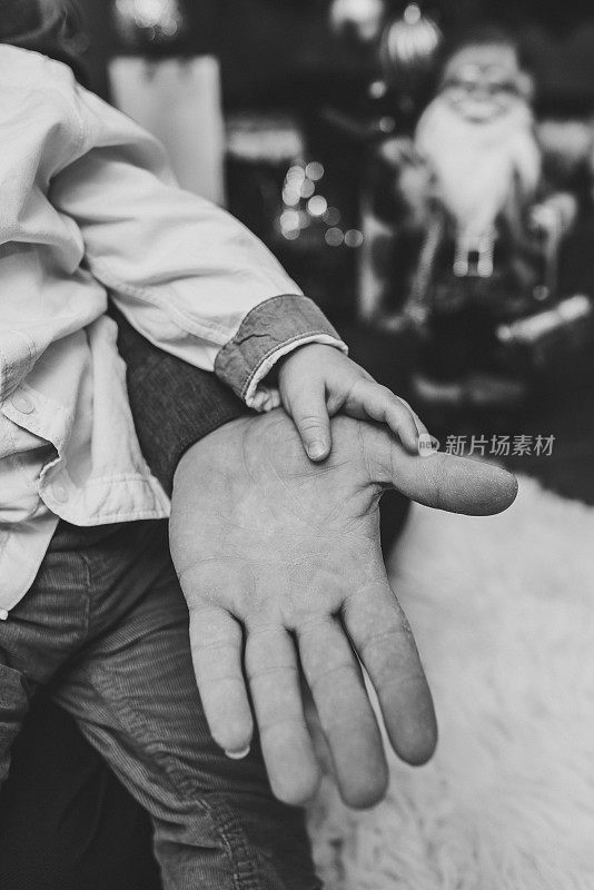 Dad and son are holding hands near a Christmas tree and a toy Santa Claus. Close up of hands. New Year and Merry Christmas. Concept of winter holiday. Ð¡old winter evenings. Black and white photo.